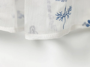 Detail von blauer Pflanzenstickerei auf halbtransparentem weißem Rüschenstoff