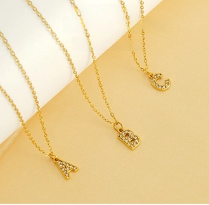 Détail de colliers dorés avec pendentifs lettres A, B et C sertis de micro-strass
