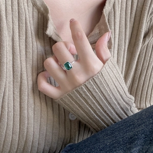 Detailed close-up of emerald-cut green gemstone ring worn on finger with soft knit sweater