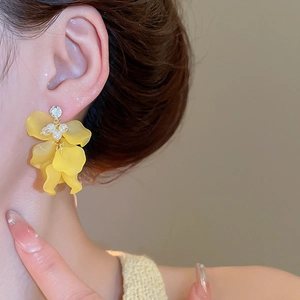 Dettaglio di orecchini a fiore gialli con perle e strass su una modella femminile