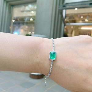 Detail of silver tennis bracelet featuring a green square gemstone on woman's wrist