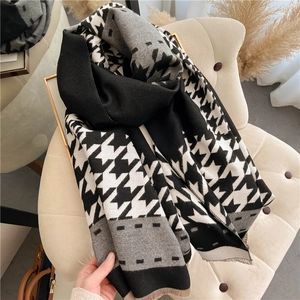 Thick warm houndstooth scarf with gray color blocking and tassels on a beige chair