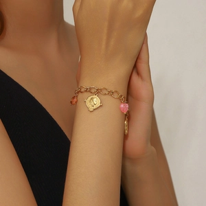 Close-up of gold-plated bracelet featuring pink heart, coin charms, and amber beads