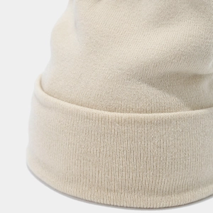 Close-up detail of soft knit texture and cuffed hem on a beige minimalist beanie