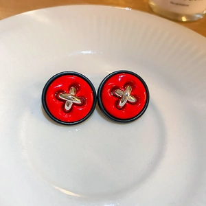 Vue macro de boucles d'oreilles bouton rouges avec bord noir et détail X argent