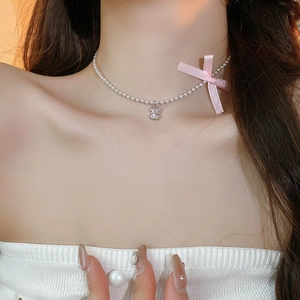 Close-up of a silver beaded necklace with a cute 3D bear pendant and a pink ribbon bow