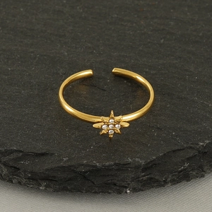 Détail d'une bague étoile en or 18k avec zircons blancs sur une texture de pierre grise