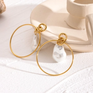 Golden stainless steel hoop earrings with baroque pearls on a textured background
