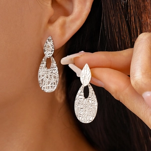 Detail of silver drop earrings with unique cracked texture on metallic surface