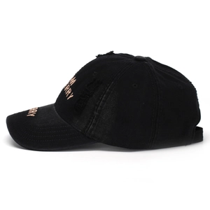 Close-up of distressed black baseball cap with golden embroidered letters and worn edge details