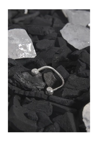 Artistic detail of silver U-shaped ring on black charcoal and clear crystal background