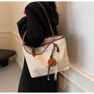 Detail of canvas tote bag with brown leather trim and cute plush bear charm accessory
