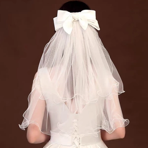 Detail of white bridal veil with satin bow and multi-layered wavy edges on a model