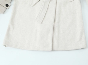 Detailed close-up of beige wool coat hem with belt and button details on sleeve