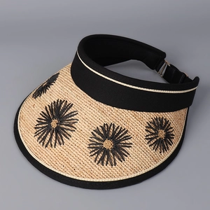 Detailed macro view of woven straw sun visor with black floral embroidery and contrast stitching