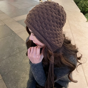 Detailed view of dark brown knitted trapper hat with braided tassels and grid texture