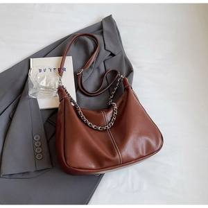 Detail of brown retro hobo bag with silver chain and white stitching on a grey blazer