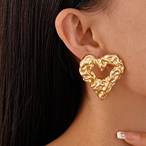 Close-up of a model wearing large golden heart earrings with wrinkled metal texture