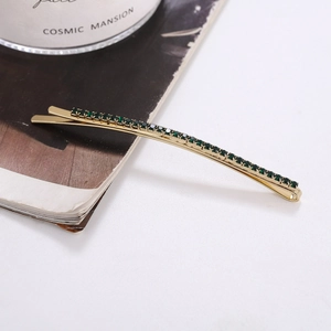 Detail of a golden metal hair clip with emerald green rhinestones on a white surface