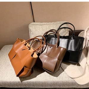 Three woven leather tote bags in caramel, dark brown, and black colors on a sofa