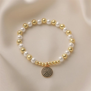 Détail du bracelet perlé avec perles nacrées, billes dorées et pendentif en zircon noir