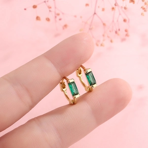 Minimalist gold hoop earrings with rectangular emerald stones shown on a hand