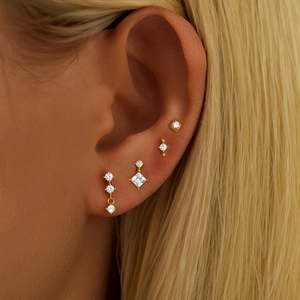 Close-up of four sparkling gold S925 silver stud earrings set on a model ear