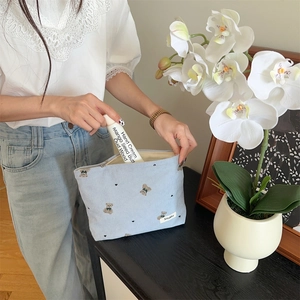 Detail of light blue corduroy makeup bag with brown bear embroidery and hand cream