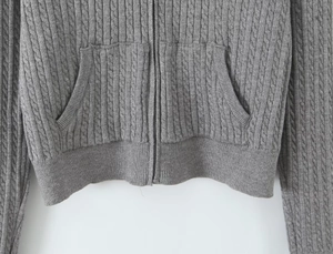 Close-up of gray cable knit hoodie featuring a front zipper and textured patch pockets