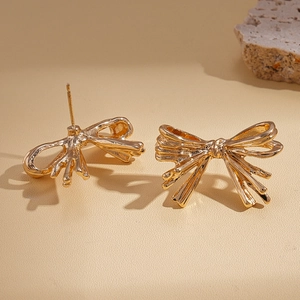 Close-up of golden ribbon bow earrings with a polished metallic finish and stud backings