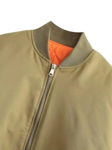 Detail of olive bomber jacket with orange quilted lining and silver metal zipper