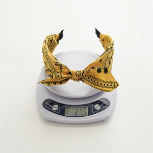 Detailed view of the 27.5g yellow knot headband with black ethnic prints on a digital scale