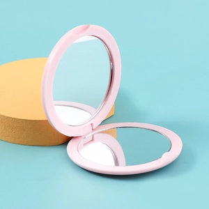 Gros plan d'un miroir de poche rond rose pliable à double face sur fond bleu clair