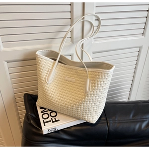 Detail of cream woven texture tote bag with slim shoulder straps on dark leather