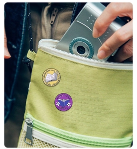 Detail of cute enamel book pins attached to a green bag for a stylish accessory look