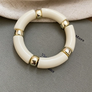 Detail of cream acrylic geometric beads with gold metal spheres on a minimalist bracelet