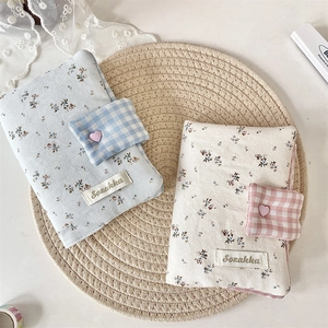 Detail of floral fabric book cover with heart button and woven label on a straw mat