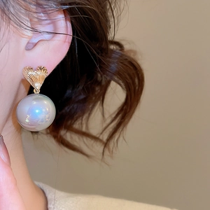Close-up of golden textured heart stud with large radiant pearl drop on ear