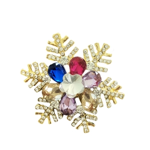 Detailed view of a gold snowflake brooch with multicolored rhinestones on a white background