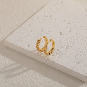 Close-up of gold cubic zirconia hoop earrings on a white textured stone display
