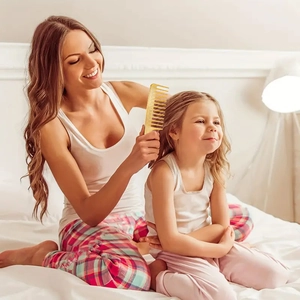 Golden wide-tooth hairbrush used by a mother for daughter's styling in a cozy setting