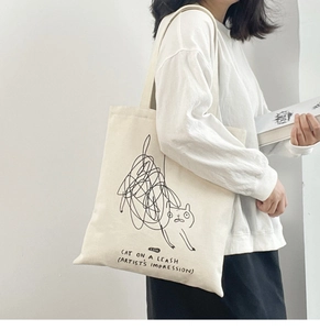 Detail view of beige canvas tote bag featuring artistic black cat doodle print on shoulder