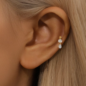 Close-up of golden 925 silver heart earring with zircon drops on a model's ear
