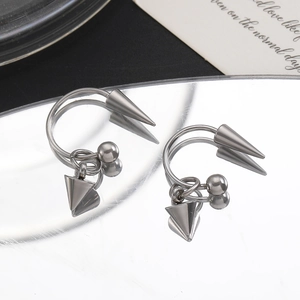 Gros plan de boucles d'oreilles punk argentées avec pointes et perles sur surface miroir