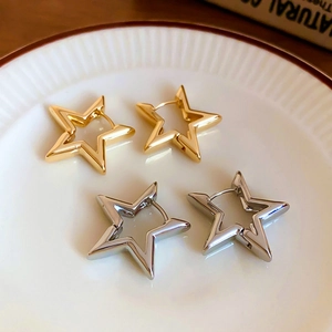 Detailed macro view of gold and silver cutout star earrings on vintage white ceramic tray