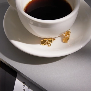 Macro shot of gold cat earrings with white rhinestone detail resting on a coffee cup