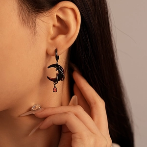 Close-up of black crescent moon and star earrings with red teardrop stone on model