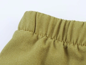 Detailed macro view of olive green linen pants featuring a wide elastic waistband and stitching