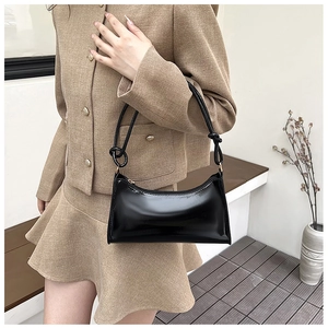 Detail of minimalist black baguette bag with glossy patent finish and knotted strap design