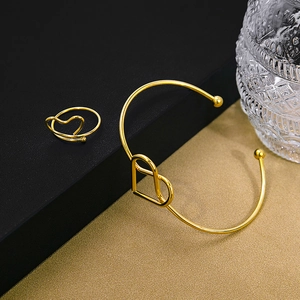 Detailed view of minimalist gold hollow heart bangle and matching ring on black leather surface